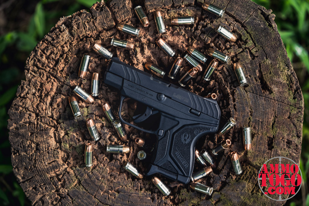 photo of ruger LCP 380 handgun with 9mm bullets on a tree stump