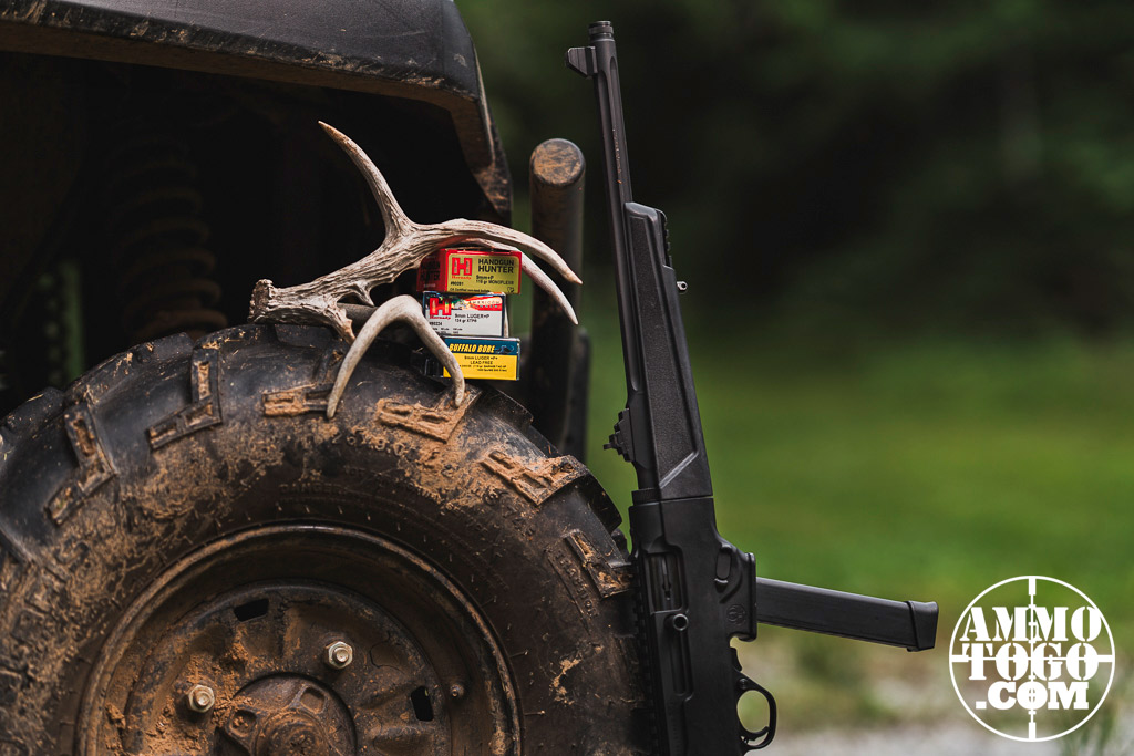 9mm ammo and a 9mm pistol caliber carbine against an ATV in the woods